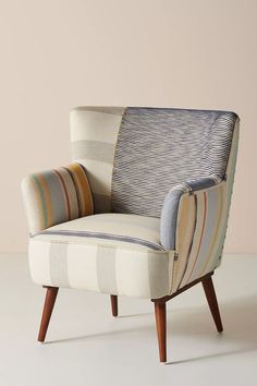 a striped chair sitting on top of a white floor next to a beige wall and wooden legs