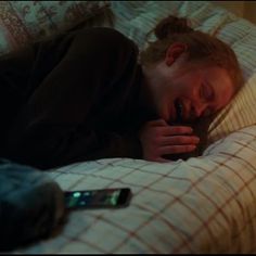 a woman laying in bed with her head on the pillow while holding a cell phone