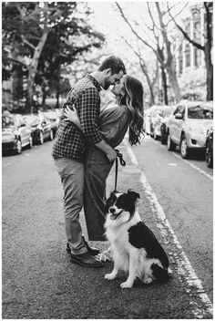 a man and woman kissing while standing next to a dog on the side of the road