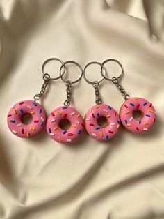 three pink donuts with sprinkles on them are hanging from key chains