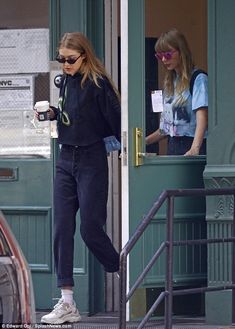 two women walking out of a building with coffee in hand and one holding a camera