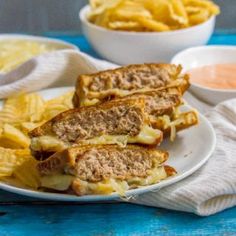 two plates filled with sandwiches and chips on top of a blue table next to bowls of potato chips