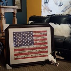 a framed american flag sits on the floor next to a black leather chair in a living room