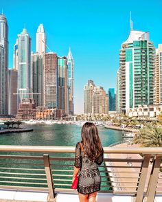 a woman is standing on a bench looking at the water in front of some tall buildings