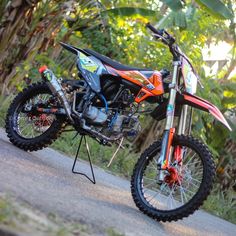 an orange and black dirt bike parked on the side of a road next to trees