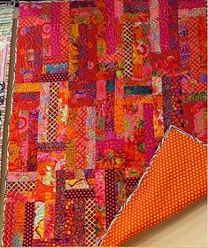 an orange and pink quilt is laying on the floor next to a piece of cloth