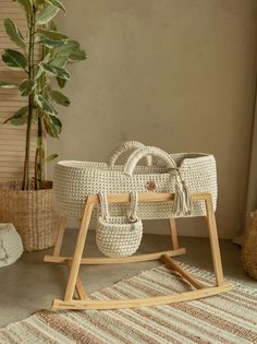 a white wicker baby's cradle sitting on top of a rug next to a potted plant