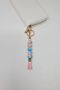 a white purse with a pink tassel hanging from it's front pocket and a gold keychain attached to it