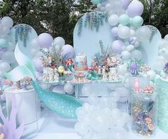 a table topped with lots of cake next to balloons and mermaid tail decorations on top of it