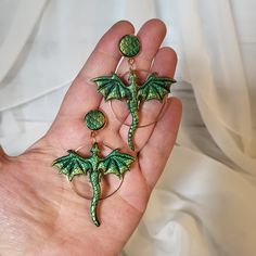 a hand holding three green dragon earrings on it's left and the other two are dangling from them