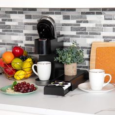 a kitchen counter with coffee cups, fruit and toaster on it's side