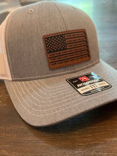 Laser engraved leather patch attached onto a Richardson trucker SnapBack.  Each hat comes with a leather matching can cooler as featured in the photos. Richardson 112 SnapBack trucker hat Leather varies slightly in color, grain and texture between each product. Leather patch hat Classic trucker cap style built with the Richardson quality and fit you've come to expect. The Richardson 112 remains a best-seller and favorite cap for teams, fans, and brands alike. Richardson 112 Fabric: Cotton-Poly/Nylon Mesh Visor: Pre-curved Sweatband: Cotton Fit: Adjustable Snapback Size: One Size Fits Most Laser Engraved Leather, Golf Hats, Gifts For Golfers, Leather Patches, Custom Leather, Trucker Cap, Dad Hats, American Flag, Laser Engraving