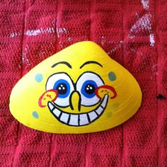 a yellow rock with a face painted on it sitting on top of a red towel