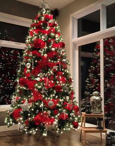 a christmas tree decorated with red and silver ornaments in front of a window at night