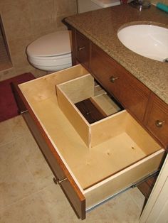 an open drawer in the middle of a bathroom counter next to a toilet and sink