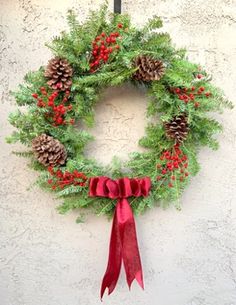 a christmas wreath hanging on the side of a building with pine cones and red ribbon