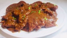 a white plate topped with meat covered in gravy and garnished with green onions