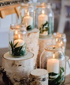 candles are in glass jars with greenery on them, and surrounded by birch logs