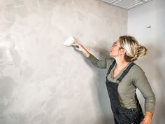 a woman is painting a wall with white paint