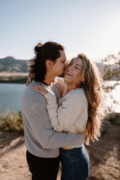 two women embracing each other in front of a lake