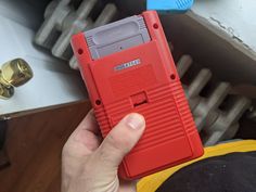 a hand holding a red nintendo gameboy case in it's left hand,