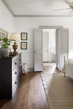 a bedroom with white walls and wood flooring has a ceiling fan in the corner