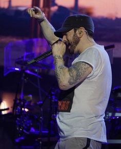 a man with tattoos on his arm holding a microphone in one hand and singing into the other