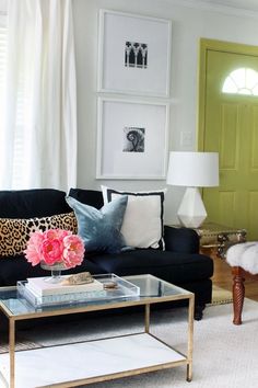 a living room with black couches, white curtains and pink flowers on the coffee table