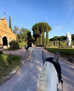 two horses are walking down the road in front of a building with statues on it