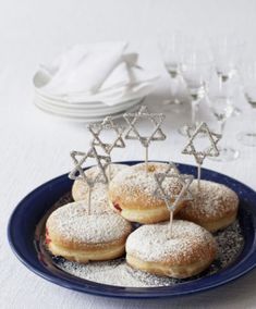 donuts with star of david on them sit in a blue plate next to wine glasses