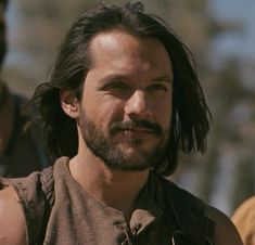 a man with long hair standing next to another man wearing a brown shirt and vest