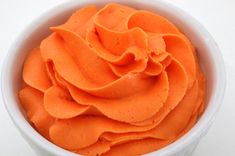 a white bowl filled with orange frosting on top of a table