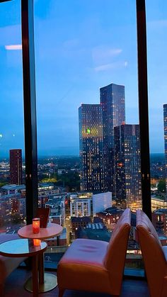 two chairs and a table in front of a large window overlooking the city at night