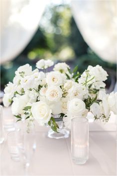 white flowers and greenery in clear vases on a table with wineglasses