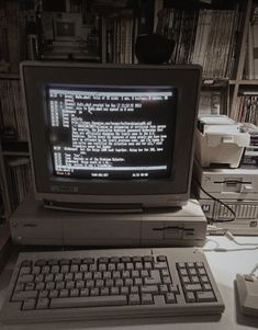 an old computer sitting on top of a desk in front of a book shelf filled with books