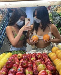 two women wearing face masks looking at apples and oranges