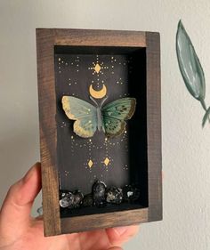 a hand holding up a shadow box with a butterfly in it's wings and stars