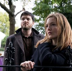 a man and woman standing next to each other in front of a fenced area