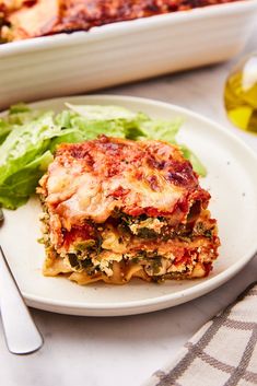 a white plate topped with lasagna covered in sauce and cheese next to a salad