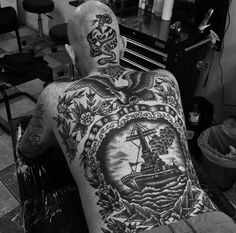 a man with tattoos on his back sitting in a chair