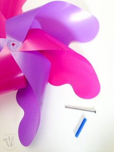 a pink and purple paper sculpture next to a blue marker on a white table top