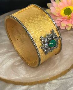 This One of a Kind textured design bangle is a beautiful piece which is set in a combination of 14kt Yellow Gold and Sterling with Pave Diamonds and Emerald. The Texturing has a beautiful scallop design and the Diamonds and Emerald is set in a Intricate Motif design. The Cuff opens from the side and the closure has Diamond Polki set on it. The Two Tone affect of the metals makes the Bangle stand out. Perfect for any look or occasion! Gross Weight : 57.72 gms 14k Gold Weight : 48.00 gms Silver We Gold-plated Bangle With Intricate Design, Multicolor Intricate Temple Jewelry Bangle, Traditional Heavy Gold-plated Bangle, Bangle Stand, Gold-plated Yellow Bangle With Intricate Design, Indian Traditional Wedding, Luxury Gold-tone Bangle With Polished Finish, Traditional Wedding Jewellery, Gold Bangles Indian