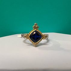 a ring with a blue stone in the center on top of a white table against a green background