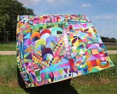 a large colorful quilt sitting on top of a lush green field