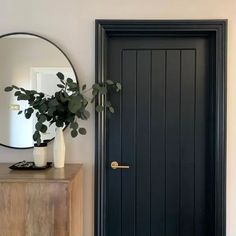 a black door with a mirror on the wall next to it and a plant in a vase