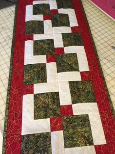 a quilted table runner with red and green squares on it's sides, along with white strips