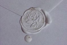 a wax seal with a rose on it and two balls in the middle, sitting on a tile floor