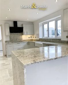 an empty kitchen with marble counter tops and white cupboards on the walls, along with large windows