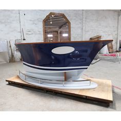 a blue and white boat sitting on top of a wooden platform in a warehouse area