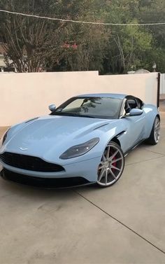 a blue sports car parked in front of a white fence with trees and bushes behind it